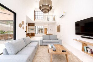 Ein modernes Wohnzimmer mit einem Ecksofa, einem Couchtisch, einem Fernseher und einem Balkon mit Pflanzen.