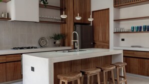 Une cuisine moderne dotée d’un îlot central, de tabourets de bar en bois, de luminaires suspendus et de meubles de rangement intégrés.