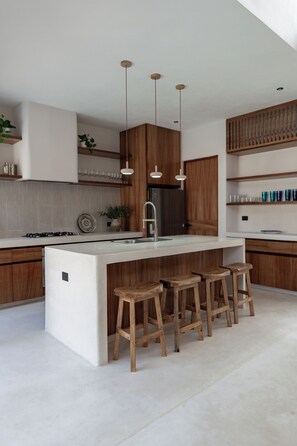 Eine moderne Küche mit einer zentralen Kochinsel, Holzbarhocker, Pendelleuchten und eingebauten Schränken.