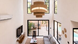 Un salon moderne avec un canapé d’angle, une table basse, un téléviseur et une grande fenêtre donnant sur un patio.