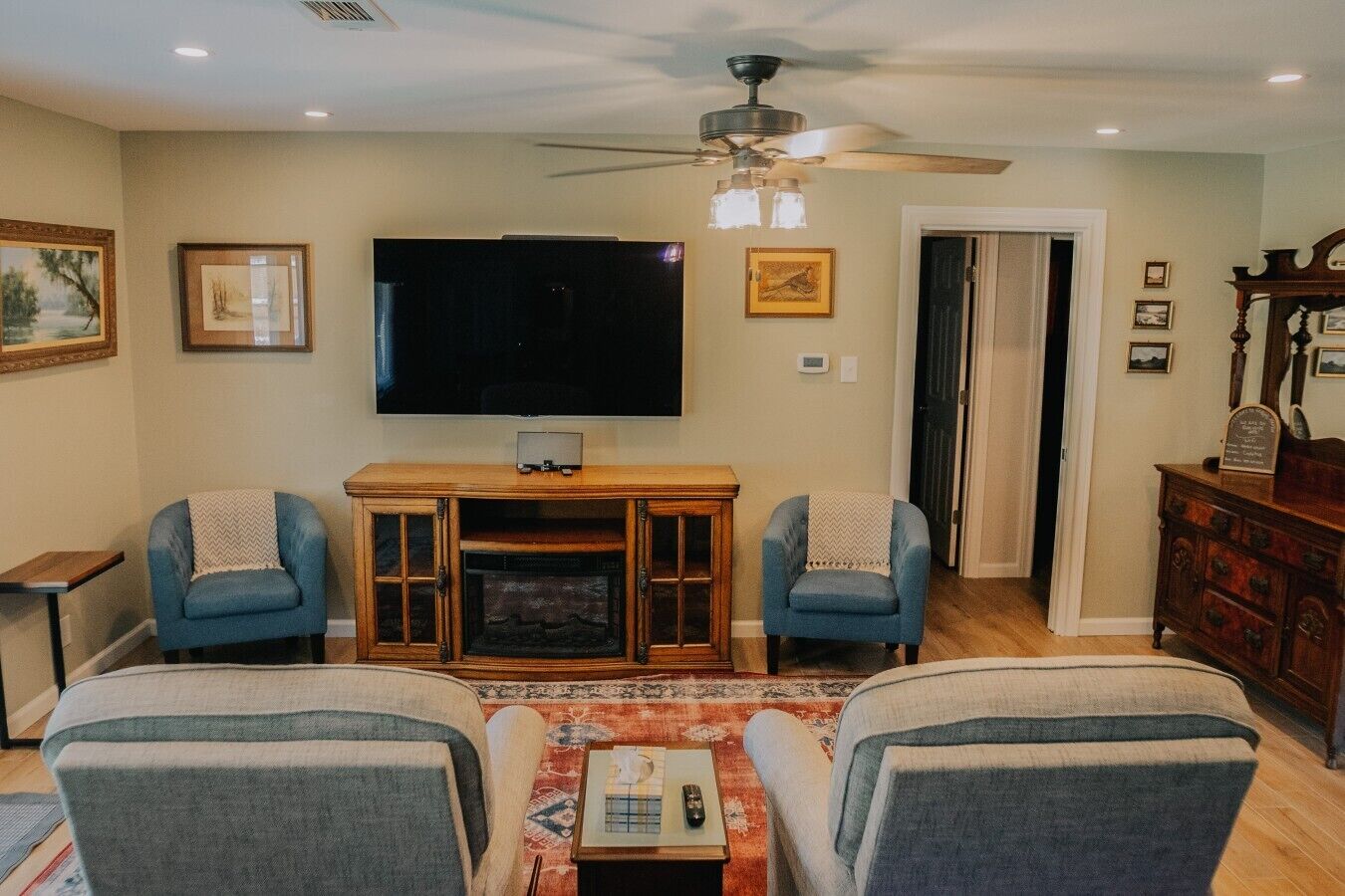 A living room with a TV, two armchairs, a fireplace, and a ceiling fan.