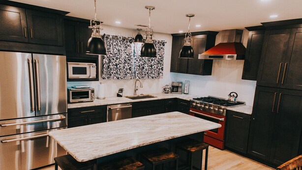 Uma cozinha moderna com armários escuros, eletrodomésticos de aço inoxidável, bancada de mármore e iluminação pendente.