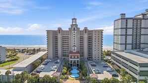 Hotel a più piani con una torre centrale, un parcheggio e vista sulla spiaggia.