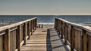 Una passerella di legno che conduce a una spiaggia, con onde e cielo sereno.
