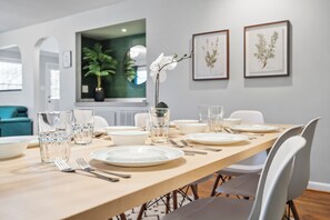 Une table à manger dressée avec des assiettes, des couverts et des verres, et des reproductions encadrées de motifs botaniques accrochées au mur.