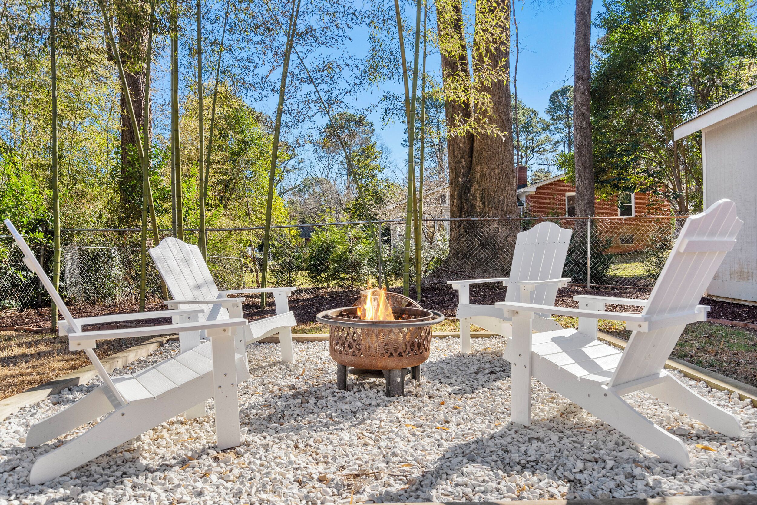 A patio area with Adirondack chairs and a fire pit surrounded by white gravel.