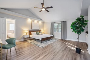 Une chambre à coucher avec un lit, un ventilateur de plafond, une plante en pot et une vue sur une salle de bain.