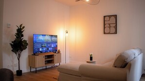 Sala de estar com televisão de tela plana, um vaso de planta, uma pequena mesa com um vaso e um sofá.
