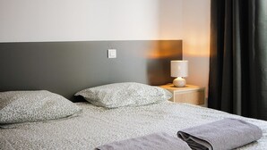 Quarto de hotel com cama, almofadas, mesa de cabeceira e cortina.
