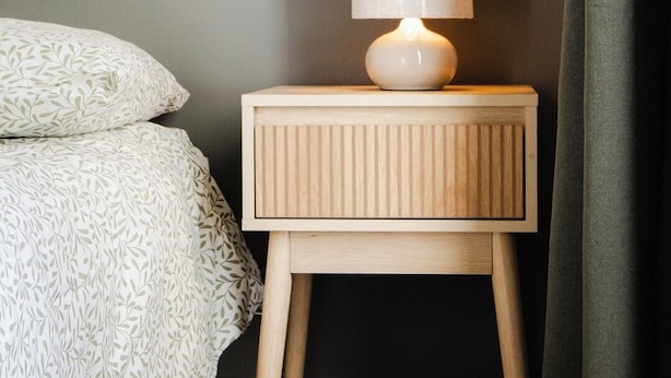 Uma cama com colcha estampada, mesa de cabeceira com abajur e cortina escura.