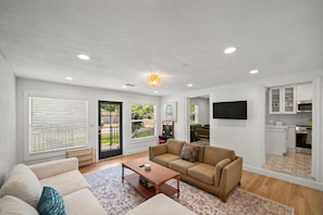 A modern living room with a beige sofa, a coffee table, and a TV mounted on the wall. - Historic Charm Near St. Pete Beach & Downtown with Arcade Games and Karaoke! (St. Petersburg)