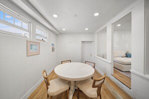 A dining area with a round table and chairs, white walls, and a view of a living room through an open door. - Historic Charm Near St. Pete Beach & Downtown with Arcade Games and Karaoke! (St. Petersburg)