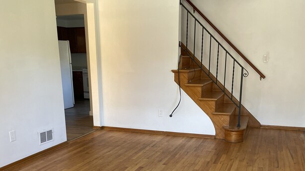 A spacious room with wooden flooring, a staircase with a metal railing, and a kitchen area in the background. - NFL Draft-Ready! 3-bedroom house in Pittsburgh (Pittsburgh)