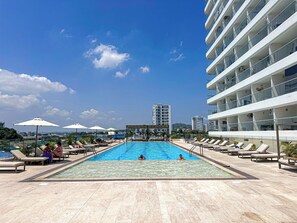 A pool area with lounge chairs and umbrellas, a clear sky, and modern buildings in the background. - Oceanfront Suite with Coworking & Pool (Cartagena de Indias)