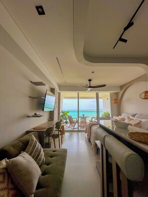 A modern living room with a sofa, a dining table, and a TV. There is a balcony with a view of the sea. - Oceanfront Suite with Coworking & Pool (Cartagena de Indias)