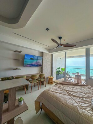 A modern bedroom with a large bed, a TV, a desk, and chairs, and a balcony with a view of the sea. - Oceanfront Suite with Coworking & Pool (Cartagena de Indias)