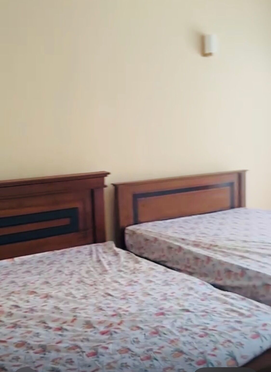 Duas camas de solteiro com roupa de cama florida, cabeceiras de madeira e luminária fixada na parede.