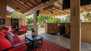 An outdoor patio with wooden furniture, a bar area, and a view of palm trees. - Modern upgraded 3-bedroom home in sunny Scottsdale! (Scottsdale)