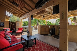 An outdoor patio with wooden furniture, a bar area, and a view of palm trees. - Modern upgraded 3-bedroom home in sunny Scottsdale! (Scottsdale)