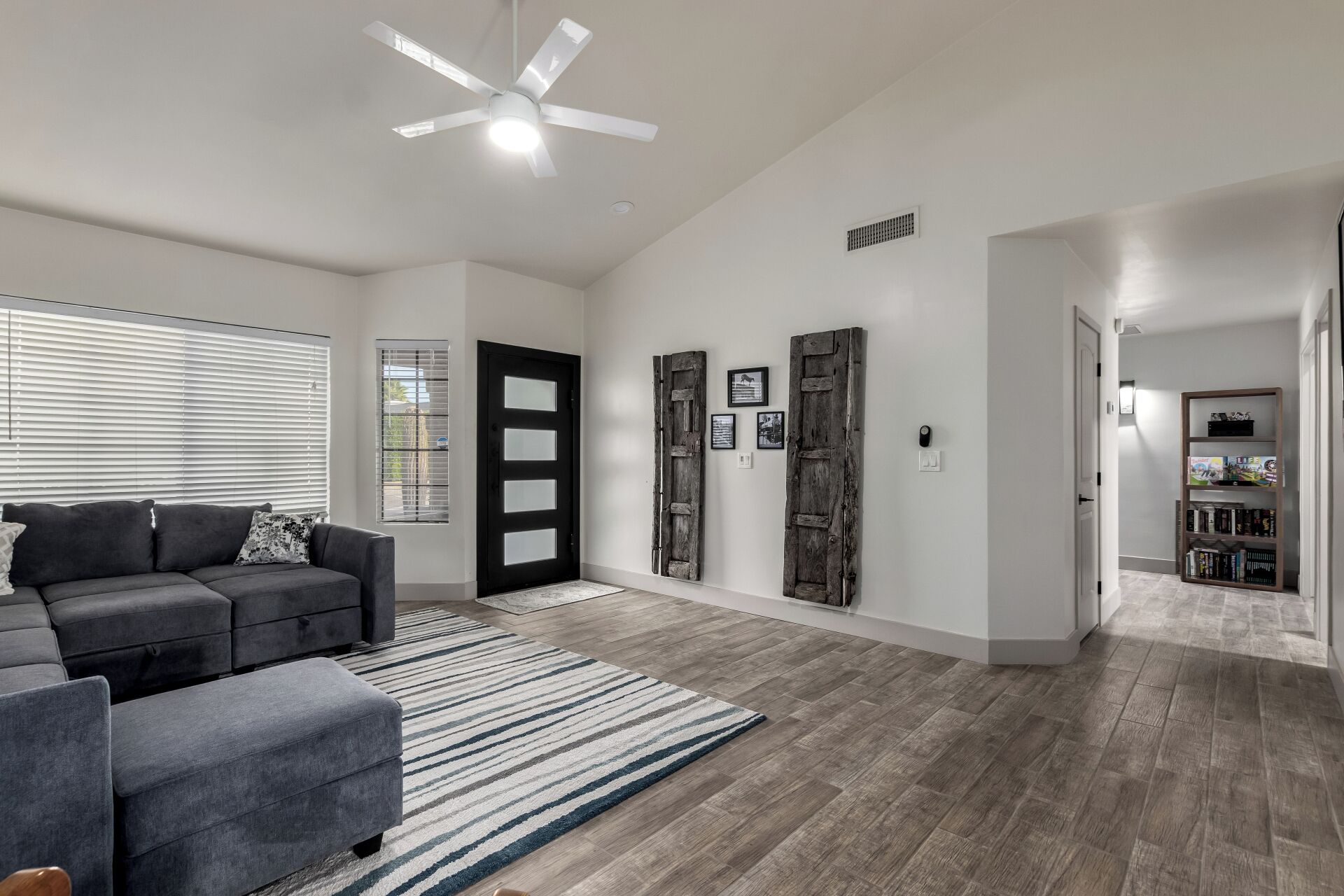 A modern living room with a gray sofa, a striped rug, and a ceiling fan.