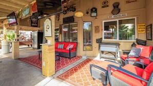 A covered outdoor seating area with wicker furniture, a red sofa, and a sign prohibiting sniveling. - Modern upgraded 3-bedroom home in sunny Scottsdale! (Scottsdale)