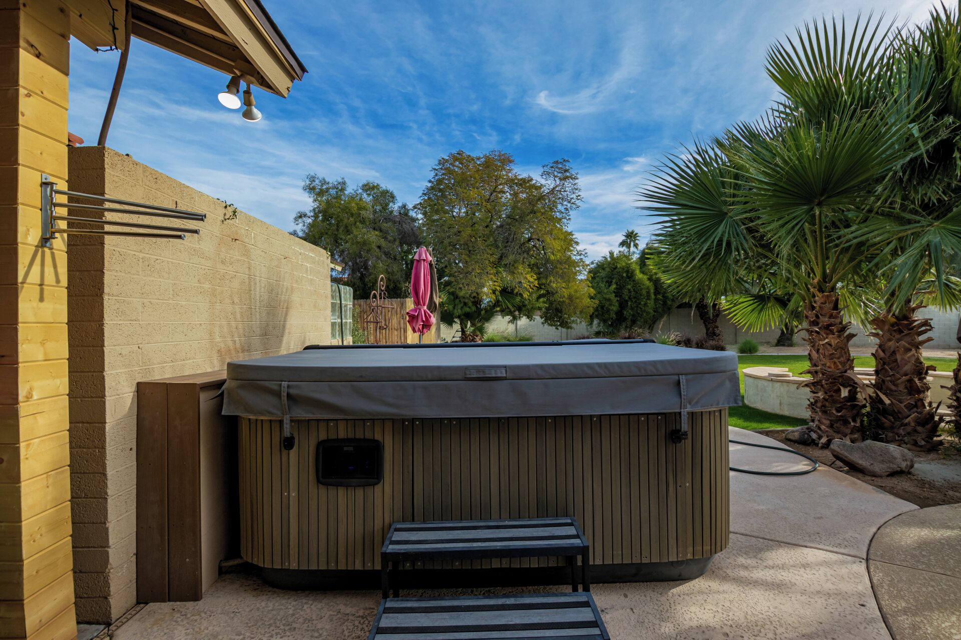 A hot tub with a bench in front, a wooden fence, and a palm tree.