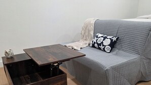 Huoneessa on harmaa sohva, puinen sivupöytä, jossa on laatikoita, ja pöydällä on pieni koriste-esine.