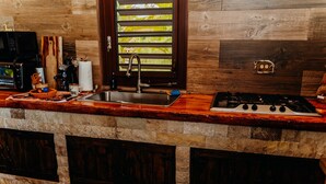 A kitchen with a stone countertop, a sink, a stove, and a window with blinds.