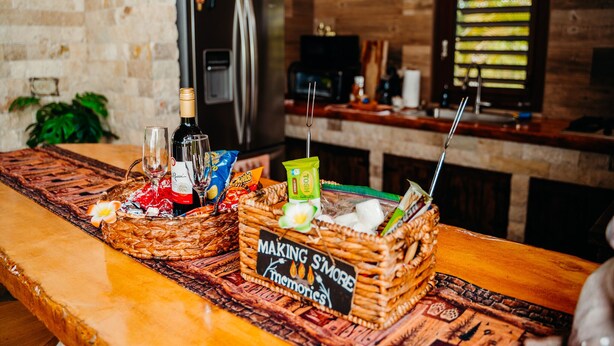 A kitchen counter with a woven basket labeled 'MAKING S'MORE memories,' containing snacks, a bottle, and a glass.
