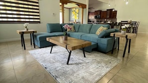 A spacious living room with a sectional sofa, a wooden coffee table, and a kitchen in the background. - Private Kingston 6 Villa w/ Pool, Swim-Up Bar & Outdoor Kitchen Near Liguanea (Kingston)