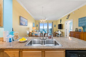 A kitchen with granite countertops, a double sink, and a dining area with a view. - Beachfront Bliss: 3-bedroom, 2-bath condo in Panama City Beach, sleeps 7. (Panama City Beach)