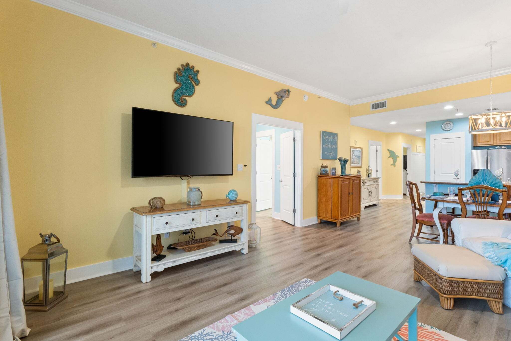 A living room with a flat-screen TV, a white console table, and a dining area with wooden chairs and a table.