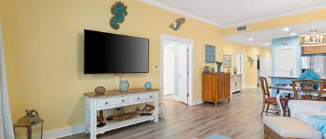 A living room with a flat-screen TV, a white console table, and a dining area with wooden chairs and a table.