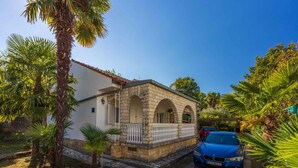 A stone building with arched windows and a balcony, surrounded by palm trees and a parked car. - Holiday apartment with terrace and barbecue (Malinska)