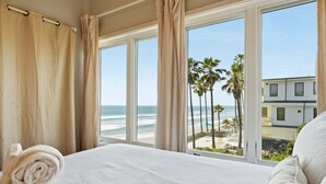 A hotel room with a bed, a view of the beach, and a building across the water. - Oceanfront Condo | Balcony, Fire Pit | Shared Beach | Sleeps 6 (Oceanside)