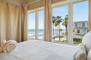 Ein Hotelzimmer mit Bett, Blick auf den Strand und einem Gebäude gegenüber dem Wasser.