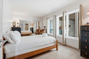 A modern hotel room with a large bed, a dresser, and a view through a window. - Oceanfront 3BR Condo | Balcony, Fire Pit | Shared Beach | Sleeps 6 (Oceanside)