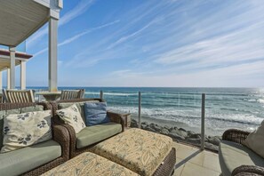 A seaside patio with wicker furniture, a view of the ocean, and a clear sky. - Oceanfront 3BR Condo | Balcony, Fire Pit | Shared Beach | Sleeps 6 (Oceanside)