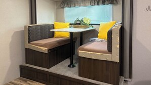 A compact RV interior with a kitchenette, two seating areas with cushions, a small table, and a window with blinds. - Perfect  1-bedroom RV getaway located in Surfside Beach.  (Surfside Beach)