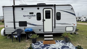 A silver RV with 'Springdale' branding, a small table, two chairs, and potted plants on a grassy area. - Perfect  1-bedroom RV getaway located in Surfside Beach.  (Surfside Beach)