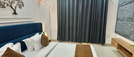A bedroom with a bed, a blue headboard, a wall-mounted lamp, a curtain, and a textured wall decoration.