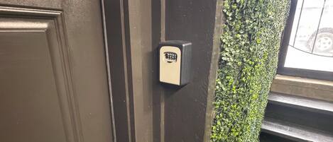 Una puerta con cerradura electrónica, una escalera con césped artificial verde y una pared cubierta de follaje verde.