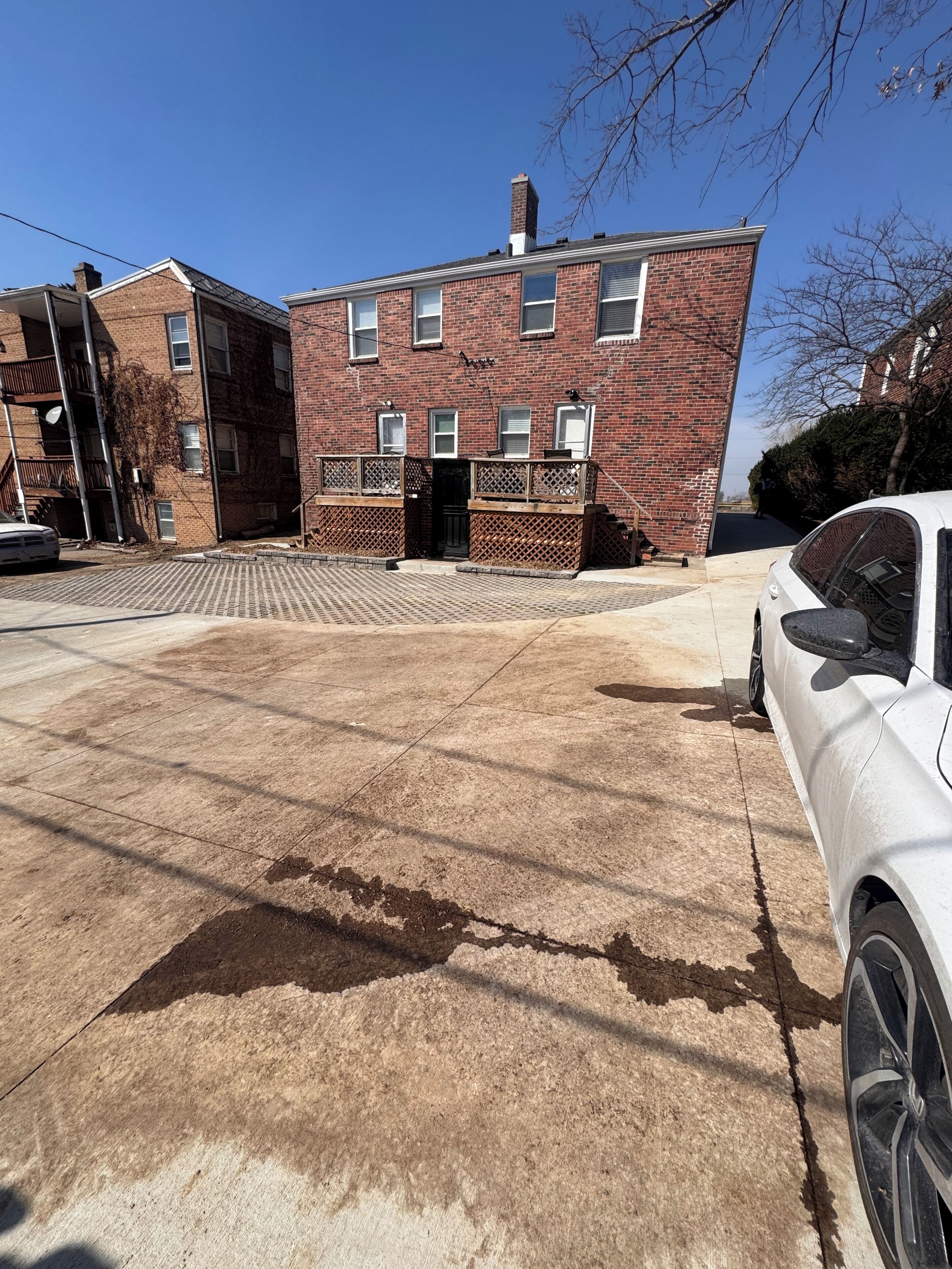 A multi-story brick building with a garage entrance, a paved driveway, and a parked white car.