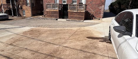 A multi-story brick building with a garage entrance, a paved driveway, and a parked white car.
