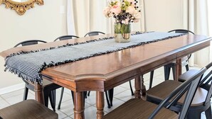 Une salle à manger avec une longue table en bois, des chaises noires, un lustre, un miroir et un vase rempli de fleurs.