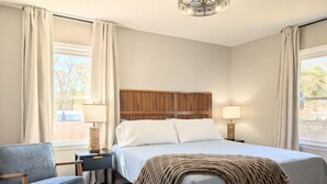 Une chambre à coucher comprenant un lit, une chaise, une table de chevet, une lampe et un luminaire au plafond.