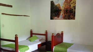 A room with three wooden beds, each with a green bedspread and white sheets. There is a painting of a landscape on the wall.