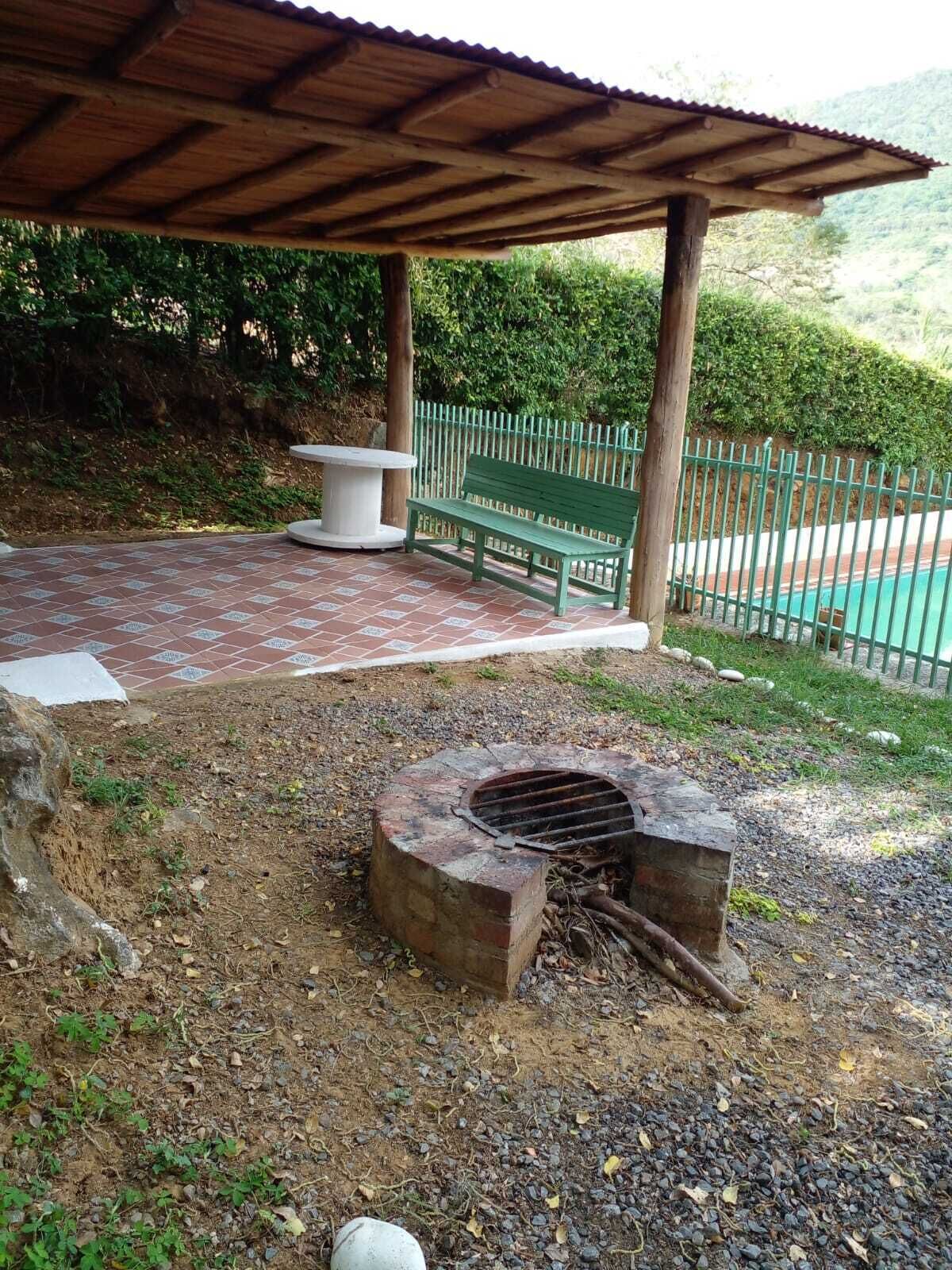 An outdoor patio with a covered seating area, a fire pit, and a pool in the background.