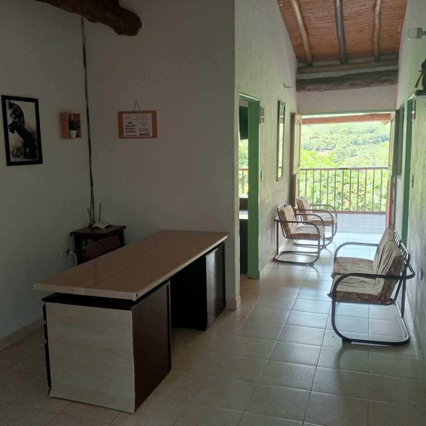 A room with a desk, chairs, a framed certificate on the wall, and a view of greenery outside.