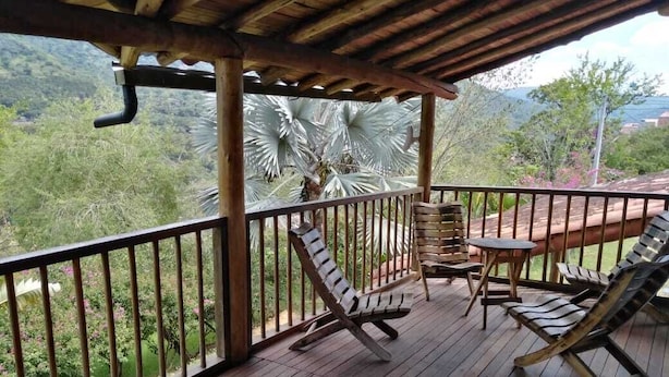 A wooden deck with a table and chairs, surrounded by a metal railing, overlooking a lush landscape.